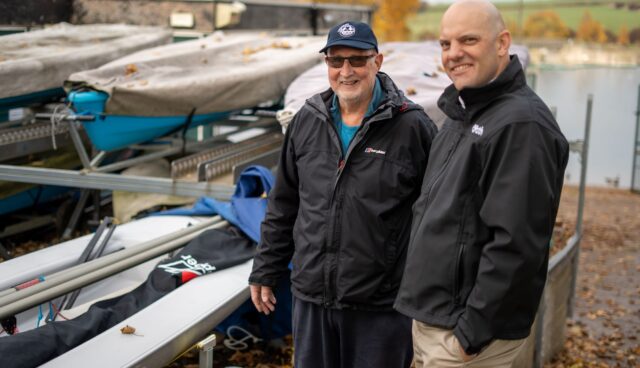 An image of commadore John from ulley Sailing club and Tom chaplin from onpath energy, standing next to some of the new boats Ulley sailing club has purchased with community fund grants