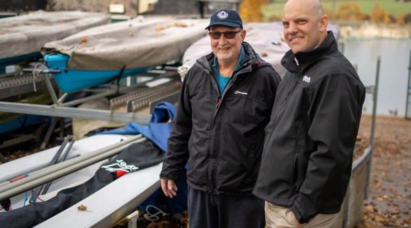 An image of commadore John from ulley Sailing club and Tom chaplin from onpath energy, standing next to some of the new boats Ulley sailing club has purchased with community fund grants